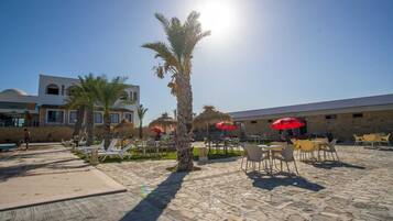 A sunny outdoor area with palm trees, outdoor seating, and a building with a dome and arched windows.