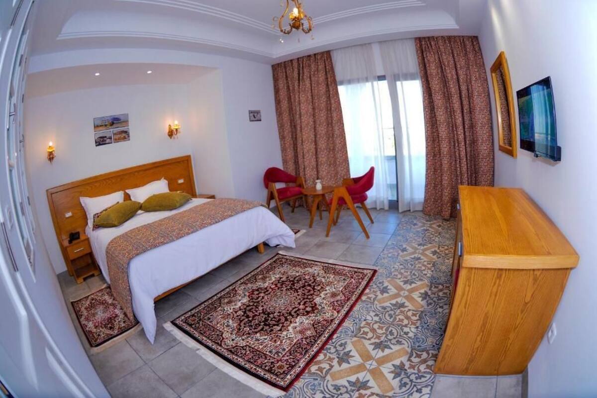 A hotel room with a bed, a desk, a chair, a rug, and curtains.