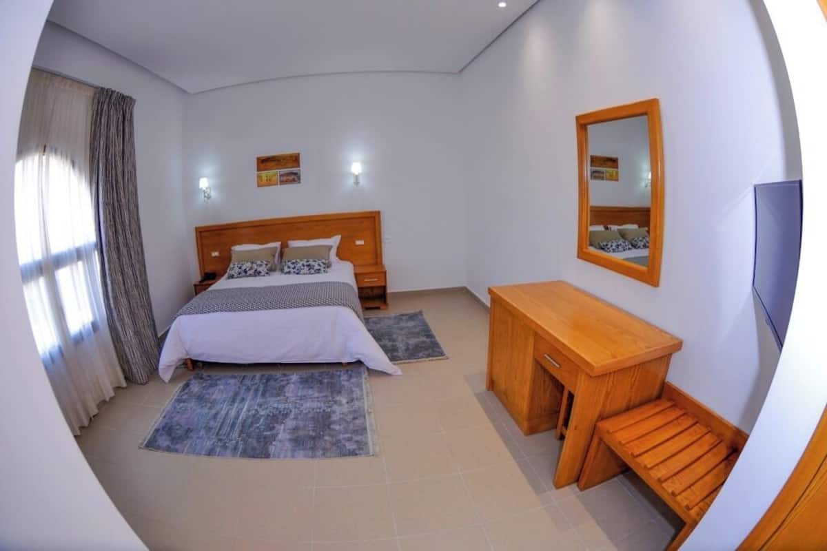 A bedroom with a bed, bedside tables, a desk, a mirror, and a TV.