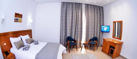 A hotel room with a large bed, two chairs, a desk, a TV, and a curtain.