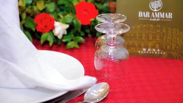 Une table dressée avec une serviette blanche, un verre à vin transparent et une cuillère posés sur une nappe rouge.