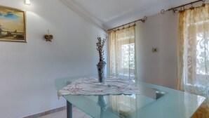 Una habitación con una mesa de vidrio, un jarrón con ramas secas y un cuadro en la pared.