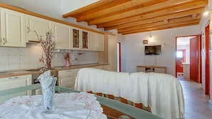 Una cocina con armarios blancos, techo de madera y un comedor con mesa cubierta con tela blanca.