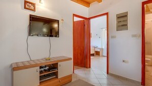 Una habitación con un televisor montado en la pared, un armario de madera con dispositivos electrónicos y una puerta que da a otra habitación.