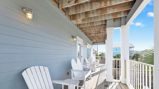 Eine Holzterrasse mit weißen Adirondack-Stühlen und einer überdachten Veranda.