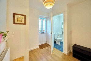Un couloir mène à une salle de bain équipée de toilettes blanches, dotée d’un plancher en bois et d’une porte ornée de vitraux.