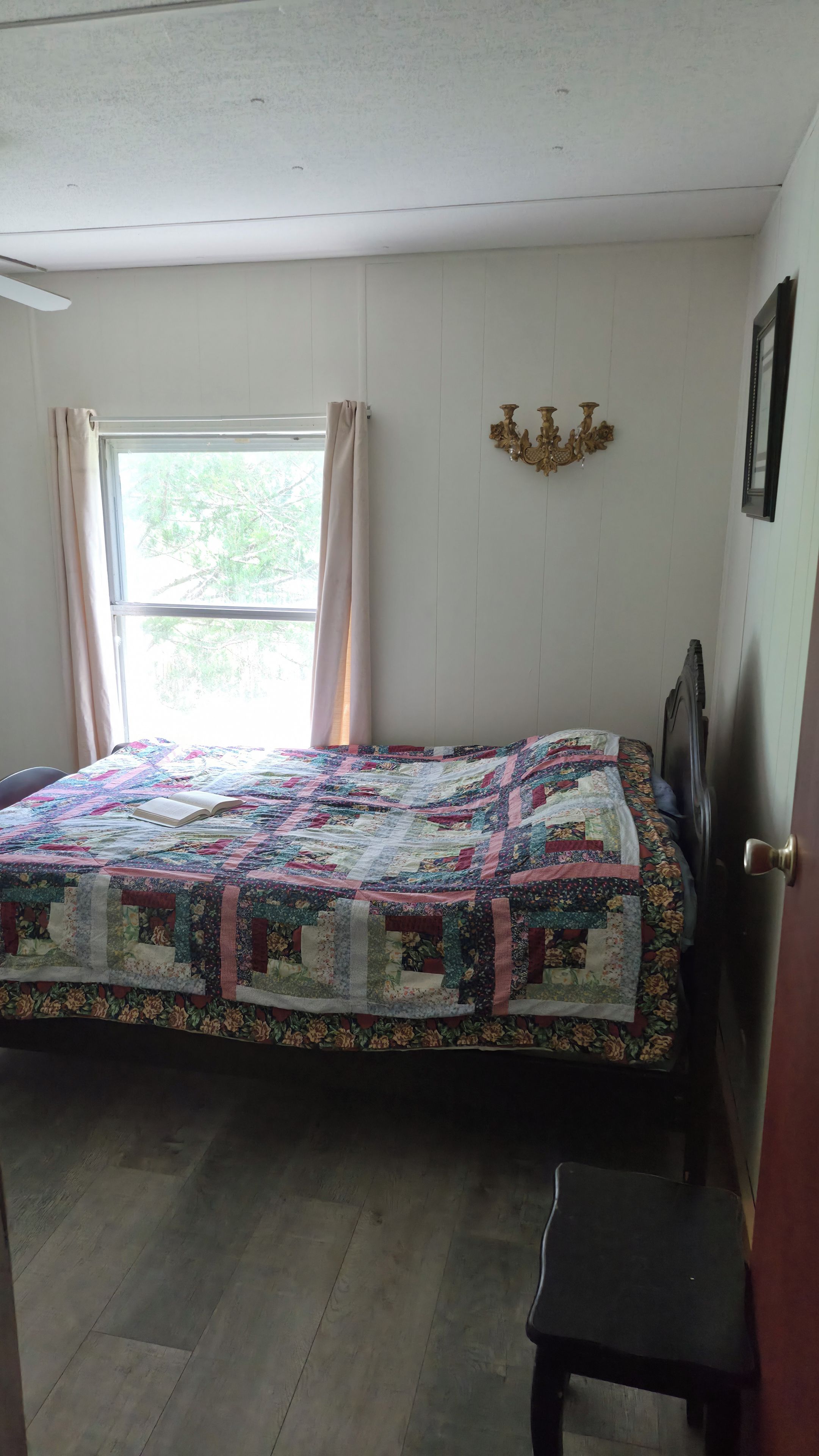 Une chambre à coucher avec un lit, une fenêtre avec des rideaux, un luminaire fixé au mur et une porte.