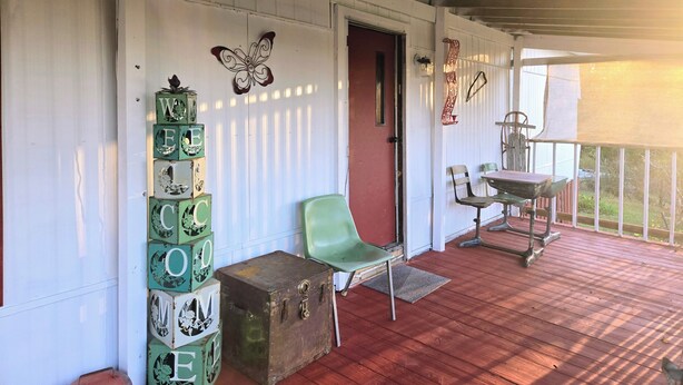 Eine überdachte Veranda mit Holzboden, einem grünen Stuhl, einem kleinen Tisch und dekorativen Blöcken, die an der Wand gestapelt sind.