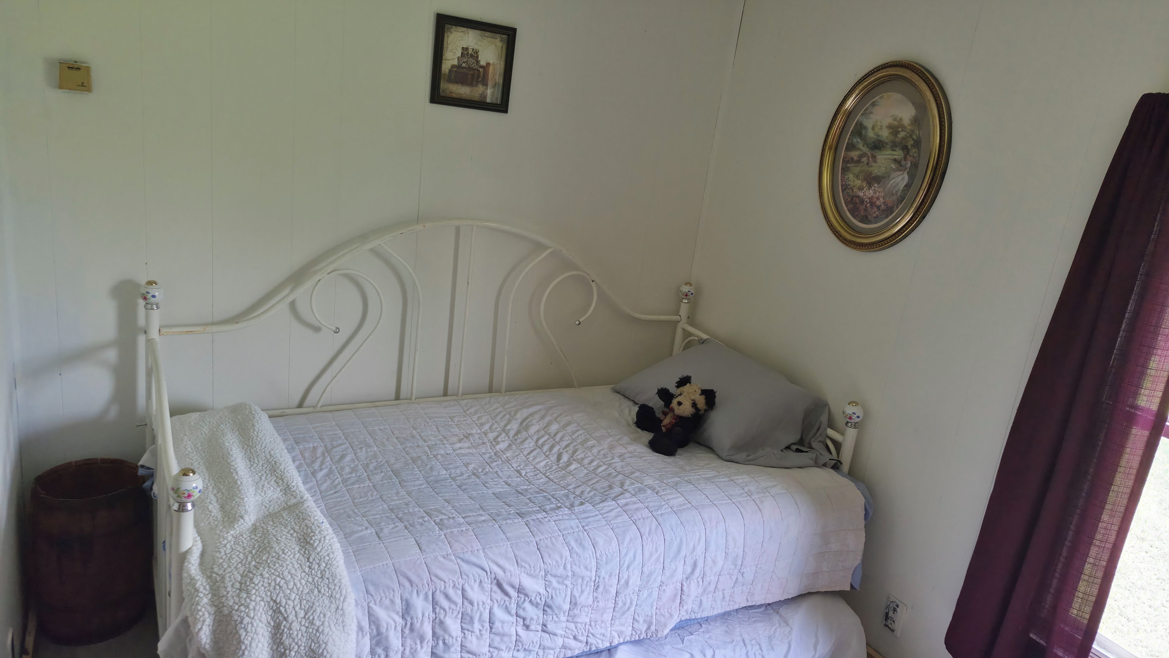 A white metal bed with a quilted mattress, a teddy bear, and a pillow on the bed.