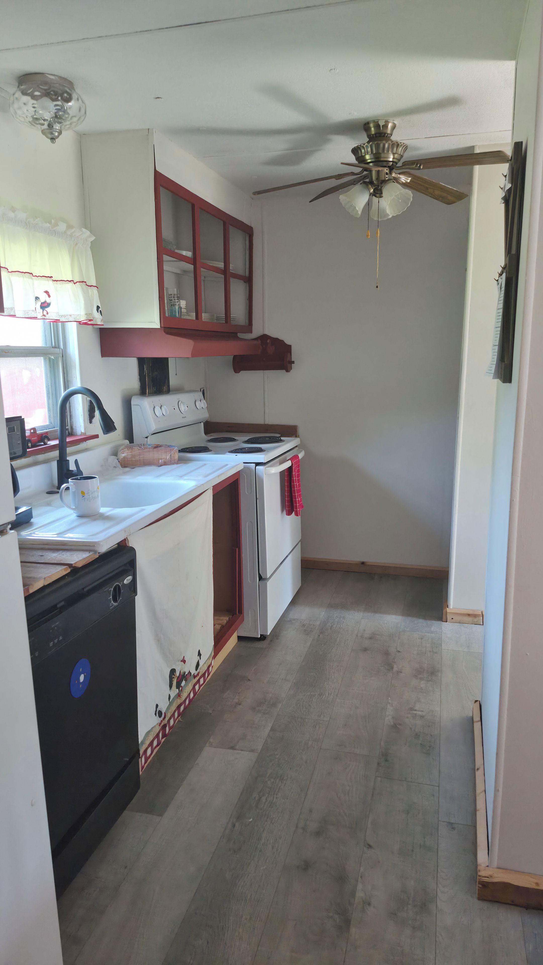 A compact kitchen with a white stove, a black dishwasher, and a red cabinet.