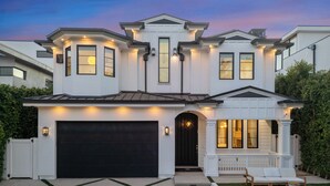 A large, two-story house with a garage, a porch with outdoor furniture, and a well-maintained lawn. - Spaulding Ave Farmhouse - Bespoke LA Home w/ Pool & Home Theater (Los Angeles)