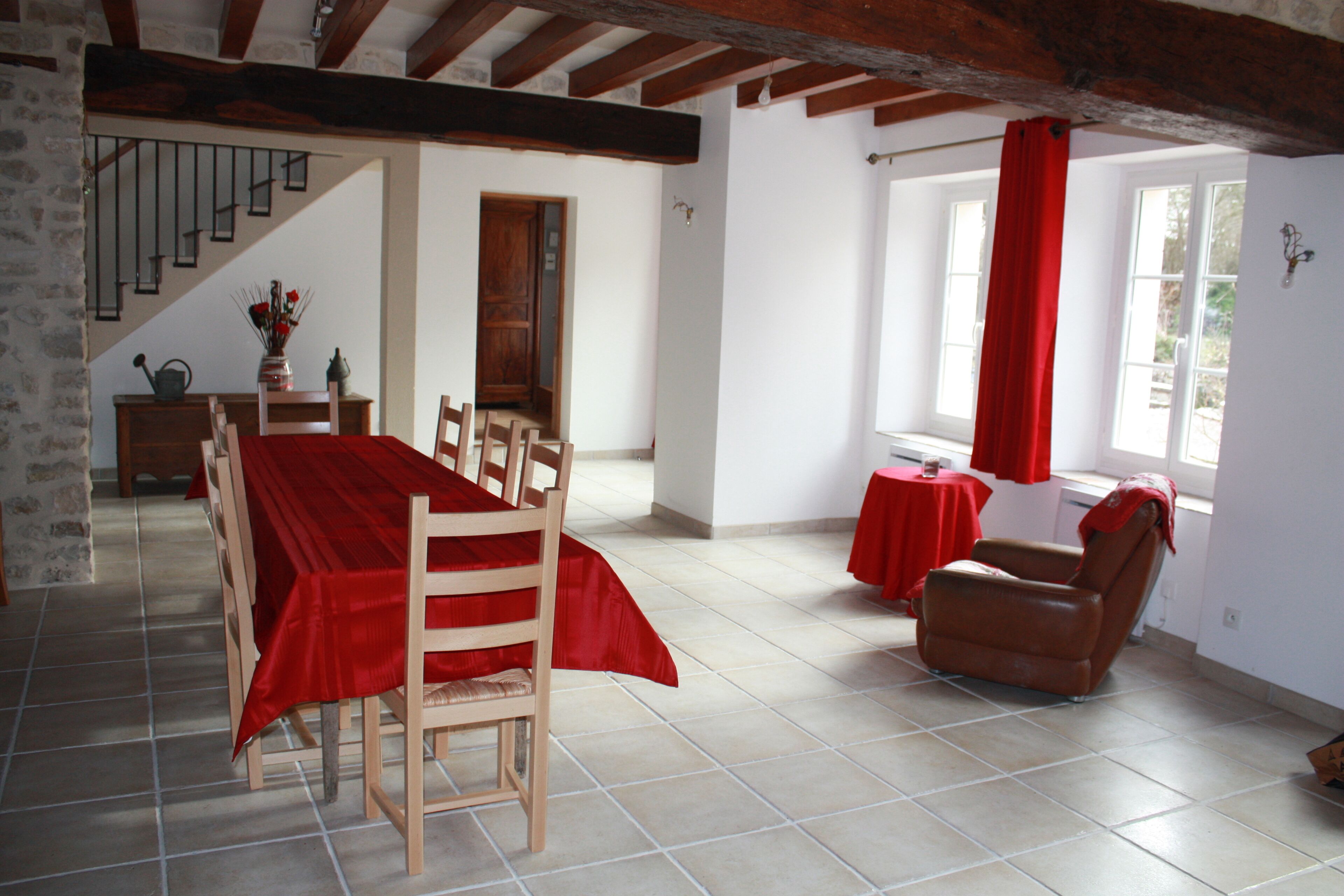 Een eetgedeelte met een houten tafel en stoelen, een trap en een rood gordijn.
