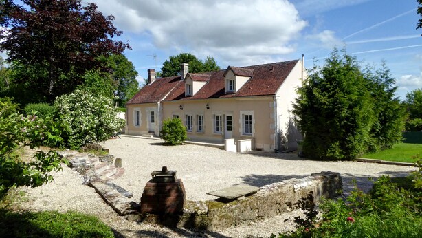 Ein zweigeschossiges Haus mit rotem Ziegeldach, umgeben von einem Schotterweg und üppigem Grün.