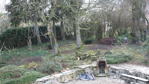 Ein Garten mit Steinelementen, einer Bank und einem kleinen Backsteinhaus.