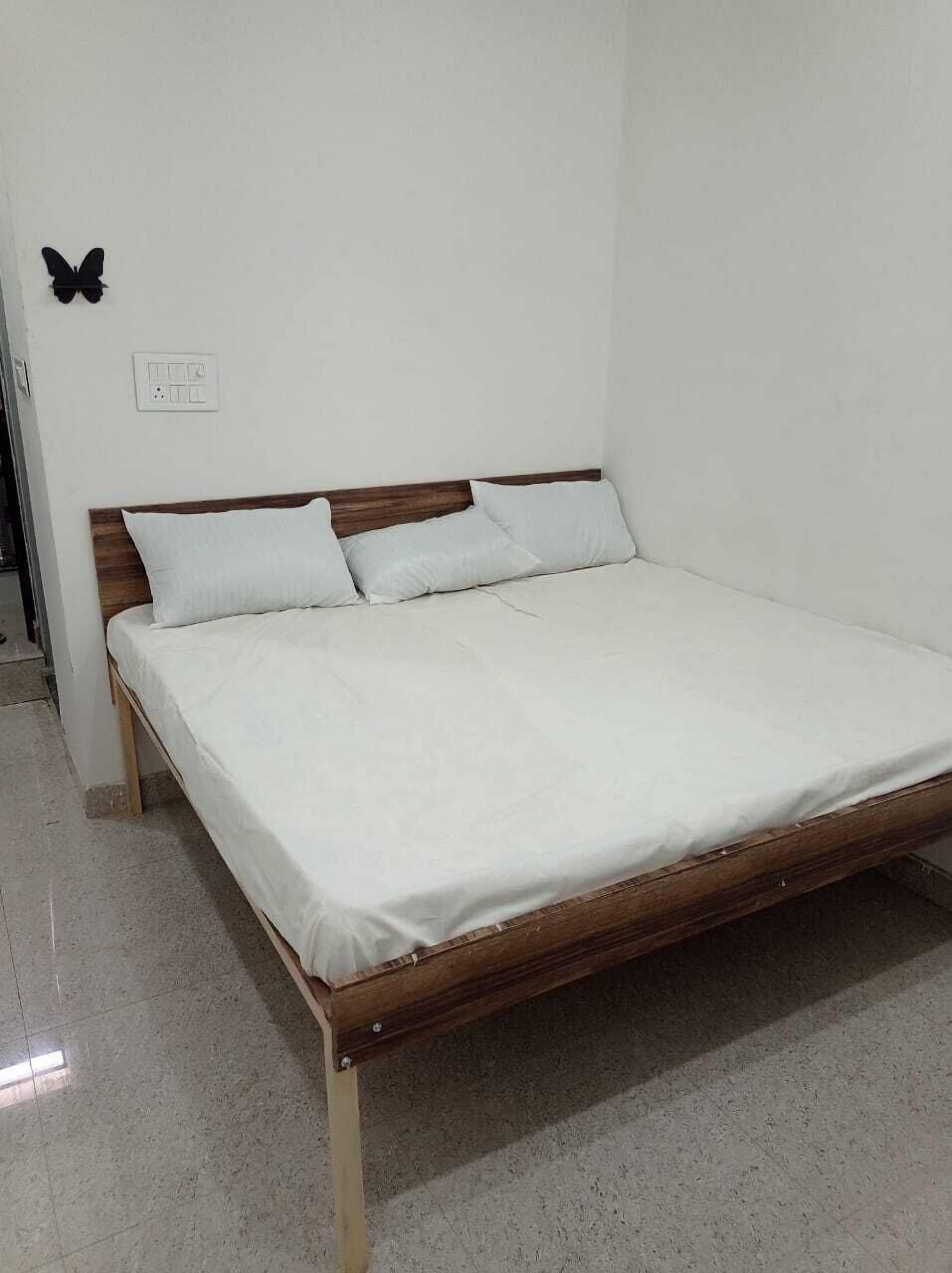 A single bed with a wooden frame and white bedding in a room with white walls and a tiled floor.