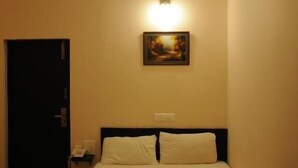 A hotel room with a bed, a ceiling fan, a wall-mounted light, and a door. - Manbhar Heavens Hotel (Amer)