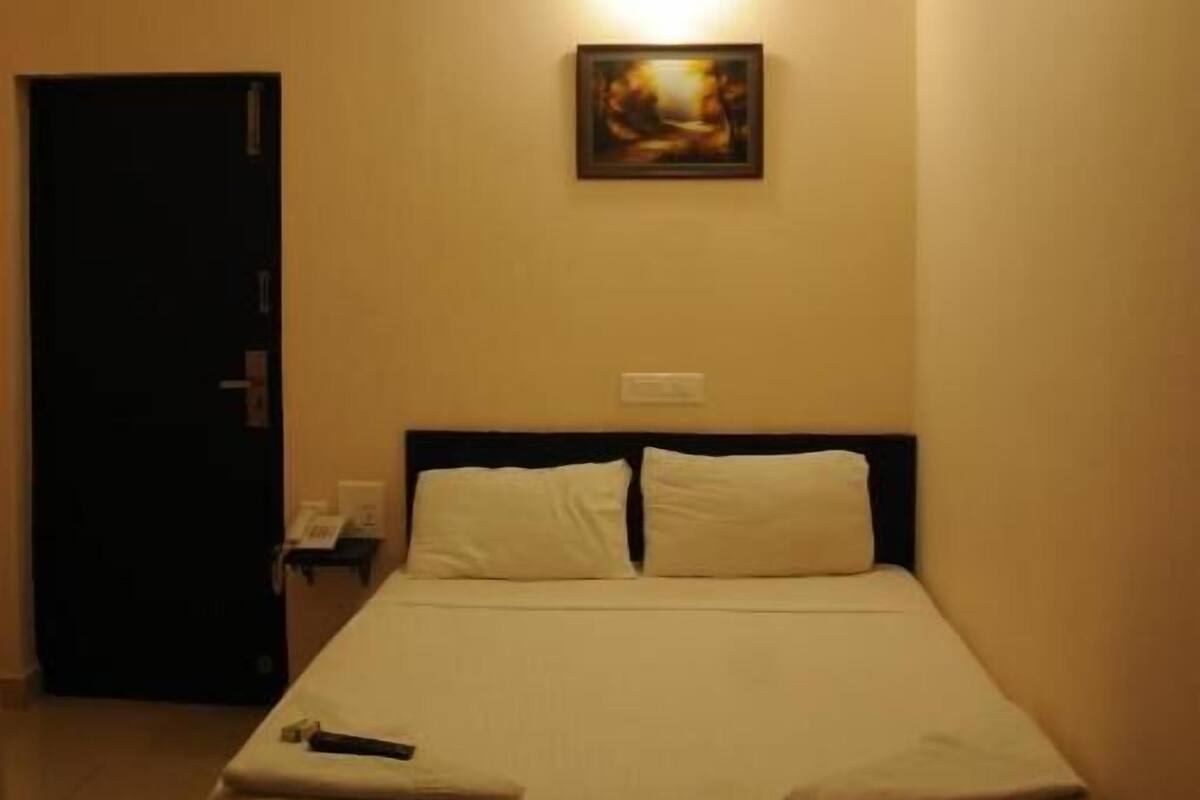 A hotel room with a bed, a ceiling fan, a wall-mounted light, and a door.