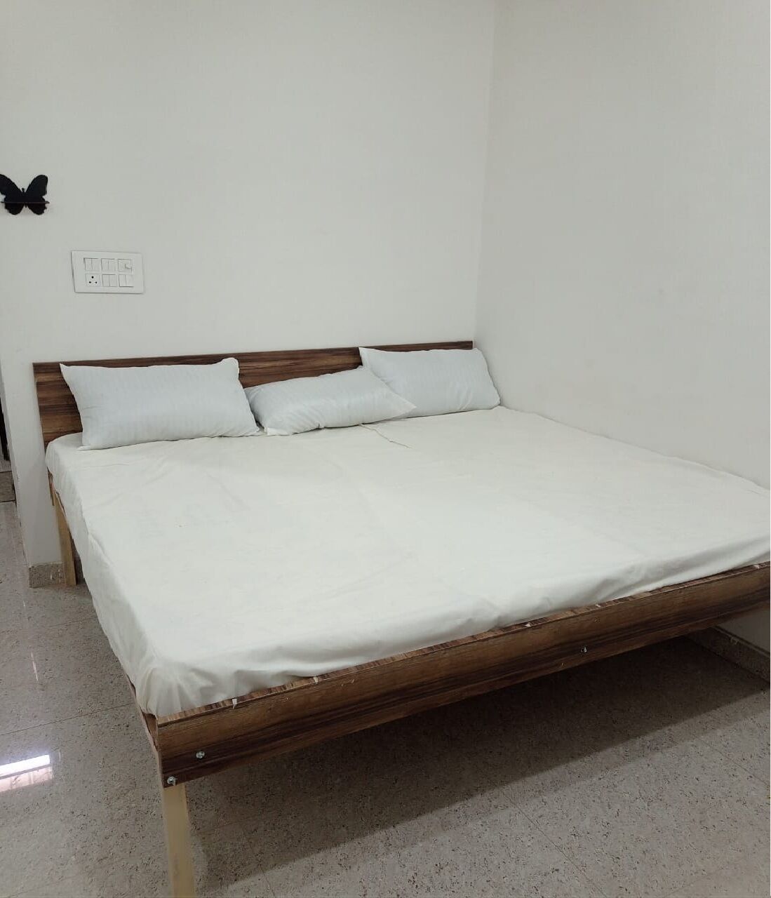 A single-bed room with a wooden headboard, white bedding, and a wall socket.