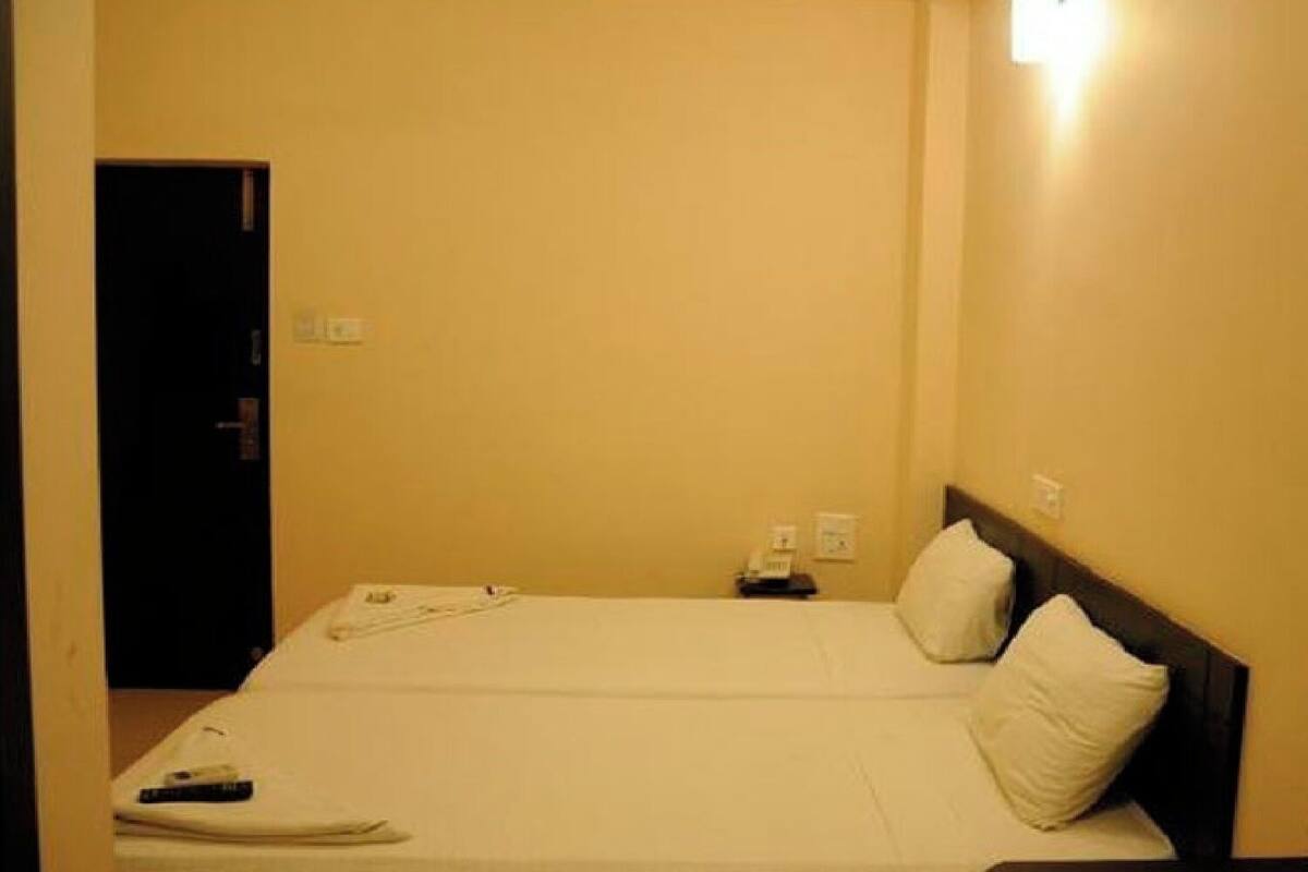 A hotel room with a bed, pillows, a bedside table, a remote control, and a door.