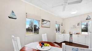 A dining area with a wooden table, white chairs, a plate of fruit, and a ceiling fan.
