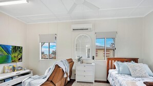 A bedroom with a bed, a chair, a dresser, a TV, and a window with a view.