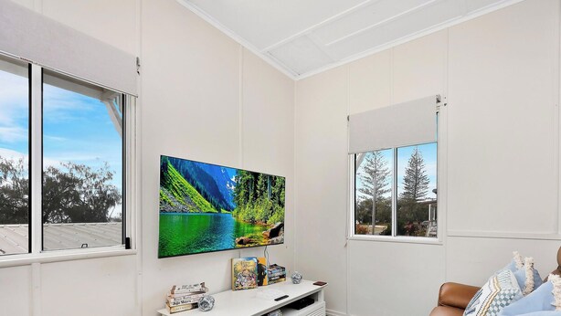 A room with a large window, a flat-screen TV, a bookshelf, and a white ceiling.