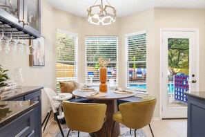 A dining area with a round table, yellow chairs, and a view of a pool through large windows. - Resort Style Backyard • Arcade Games • Hot Tub (San Antonio)