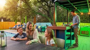 A poolside area with a covered seating area, a barbecue station, and lounge chairs. - Resort Style Backyard • Arcade Games • Hot Tub (San Antonio)