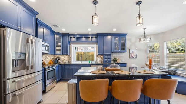 Een moderne keuken met blauwe kastjes, roestvrijstalen apparatuur en een centraal eiland met zitplaatsen.