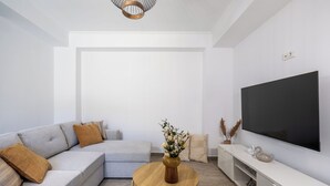 Moderni olohuone, jossa on harmaa kulmasohva, pyöreä puinen sohvapöytä, seinälle asennettu taulutelevisio ja minimalistinen sisustustyyli.