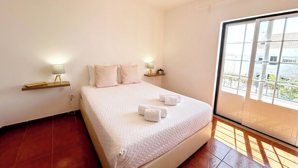 Un dormitorio con una cama grande, dos mesitas de noche con lámparas, una ventana con vistas a edificios y una lámpara de techo roja.