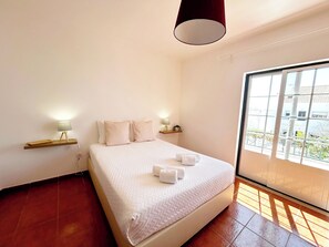 Un dormitorio con una cama grande, dos mesitas de noche con lámparas, una ventana con vistas a edificios y una lámpara de techo roja.