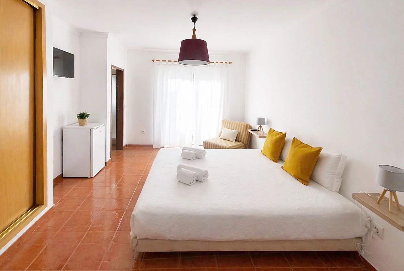 A hotel room with a large bed, a desk, a chair, a TV, and a window with curtains.