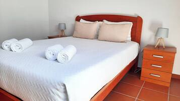 Una cama bien hecha con toallas blancas enrolladas, un cabecero de madera y una mesita de noche con lámpara.
