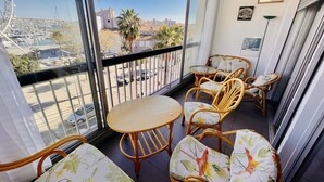Ein Balkon mit Korbmöbeln, einem runden Tisch und Blick auf einen Yachthafen und Gebäude.