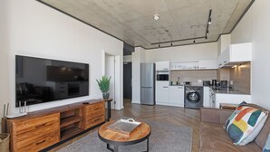 A modern living room with a large TV, wooden entertainment unit, and a round coffee table. - Central Century City Comfort | Balcony and Wi-Fi (Cape Town)