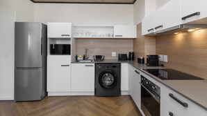 A modern kitchen with a stainless steel refrigerator, a built-in washing machine, and a sleek countertop. - Central Century City Comfort | Balcony and Wi-Fi (Cape Town)