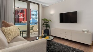 A modern living room with a sofa, a coffee table, a TV, and a view of a balcony with buildings. - Dolce Vita | Stylish Sea Point Gem (Cape Town)