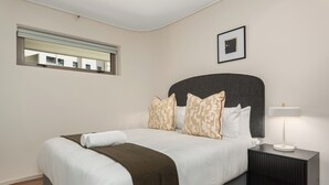 A neatly made bed with patterned pillows, a bedside lamp, and a framed picture on the wall. - Dolce Vita | Stylish Sea Point Gem (Cape Town)