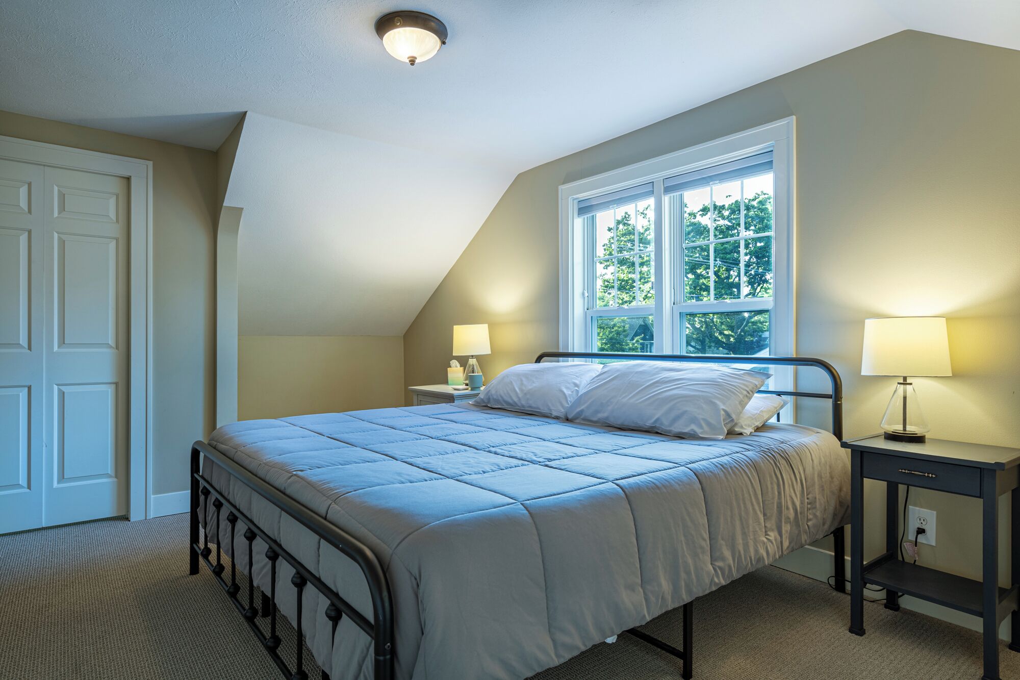 A bedroom with a bed, two bedside tables with lamps, a window, and a door.