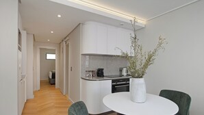 Eine moderne Küche mit weißen Schränken, einer Granit Arbeitsplatte und einem eingebauten Backofen. Ein Essbereich mit einem weißen Tisch und zwei grünen Stühlen ist ebenfalls vorhanden.