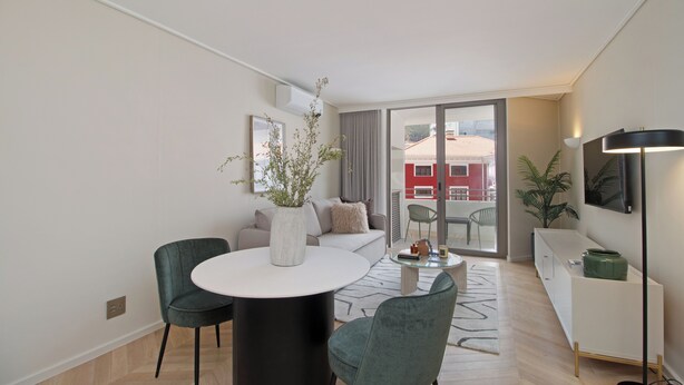 Ein modernes Wohnzimmer mit einem runden Esstisch, zwei Stühlen, einem Sofa, einem Fernseher und einer Pflanze.