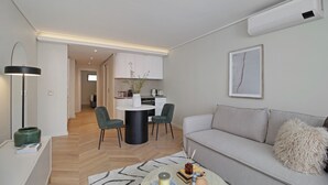 Ein modernes Wohnzimmer mit grauem Sofa, einem Couchtisch und einem Essbereich mit weißem Tisch und Stühlen.
