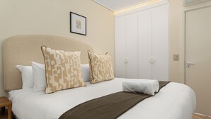 Cama bem arrumada com almofadas estampadas, um cobertor marrom e um quadro na parede.