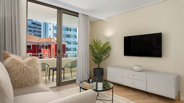 Uma sala de estar moderna com sofá, mesa de centro de vidro, televisão e planta em vaso.