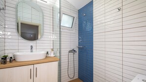 Een badkamer met een witte wastafel, houten opbergmeubel, een spiegel, een douche met een blauwe wand en een toilet.