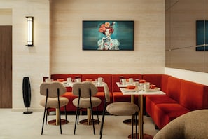 A modern dining area with a red booth, wicker chairs, and a table set for two. - Jills Hotel (Paris)
