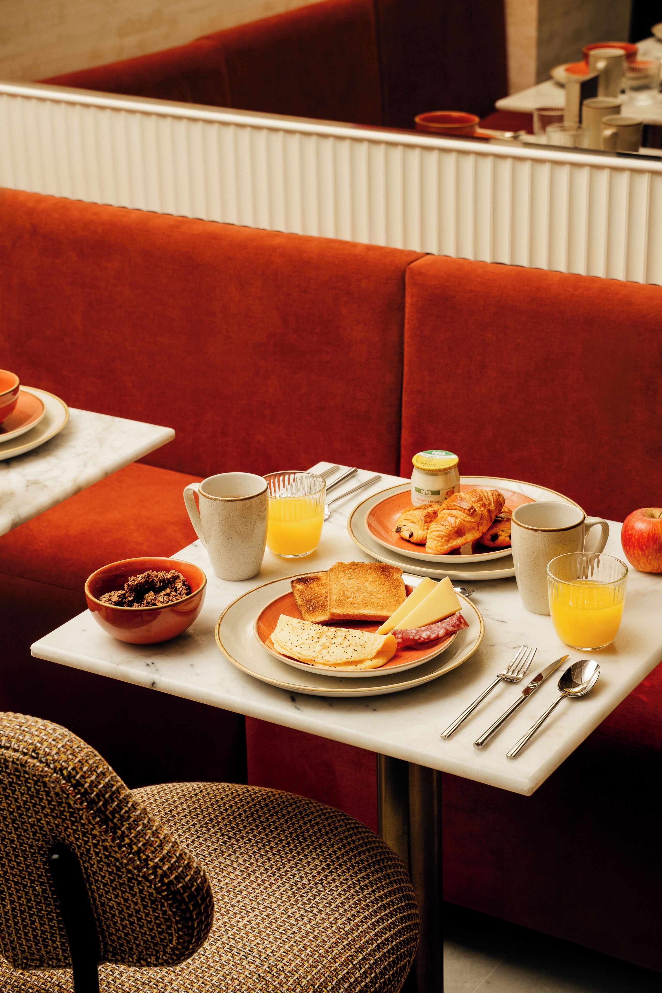 A breakfast setting with a table, red upholstered booth, and various breakfast items.