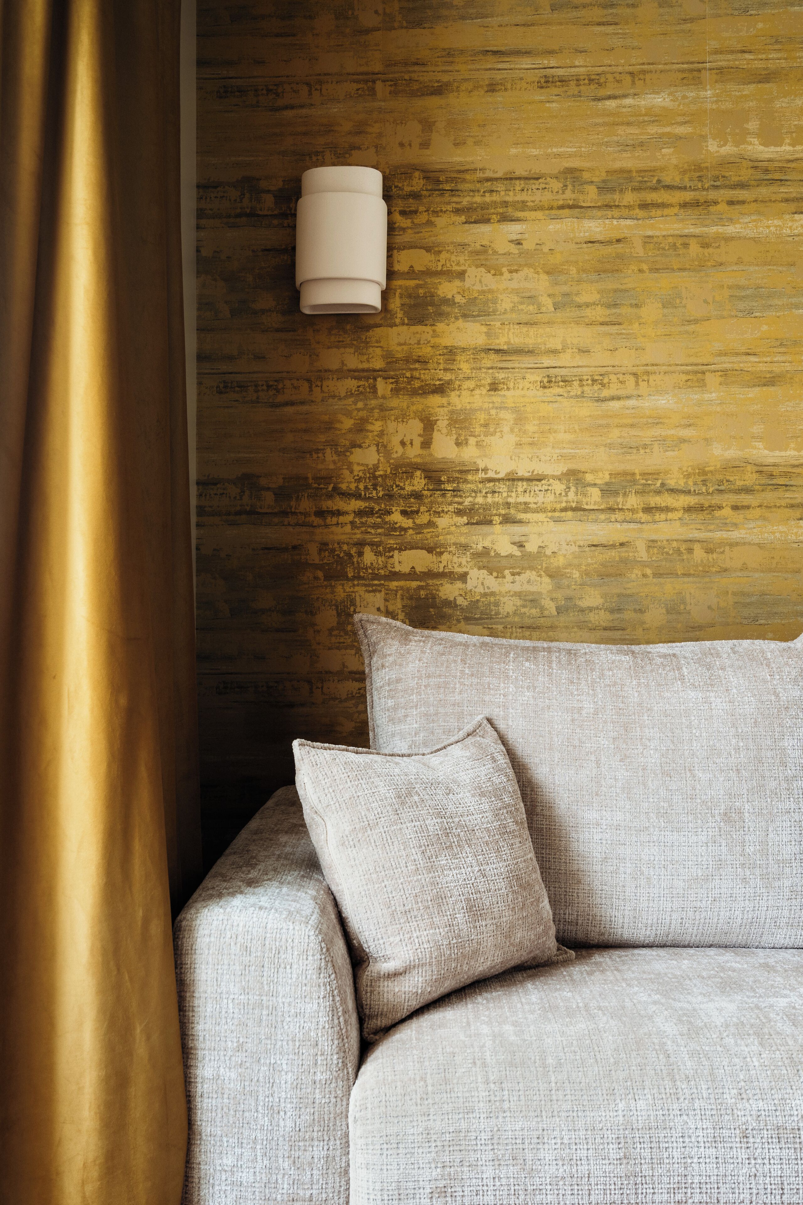 A room with a textured wall, a sofa with pillows, and a wall-mounted light fixture.