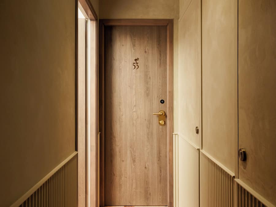 Un couloir étroit avec une porte en bois, des murs de couleur beige et un radiateur sur le côté gauche.